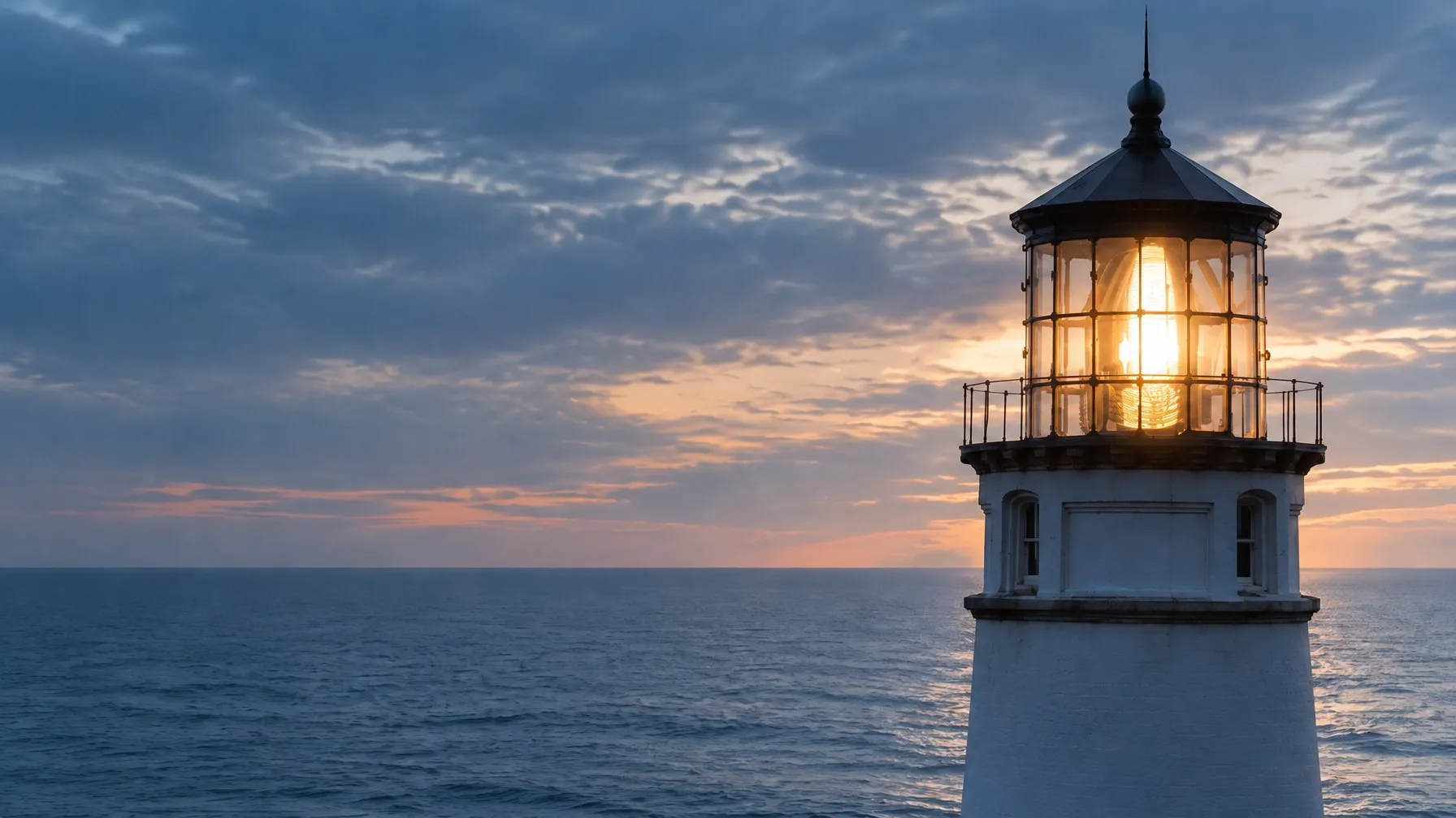 A lighthouse shining over a calm ocean at dusk